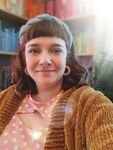 white person with brown hair and blue headband with neutral smile in front of multi colored bookcase